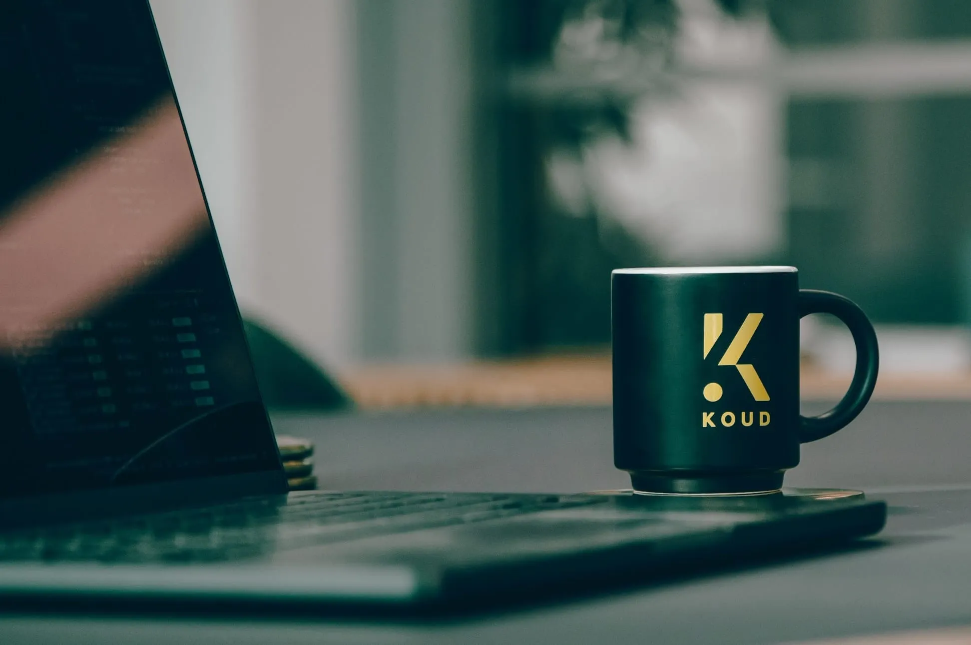 Koud-kahvimuki kannettavan vieressä, jonka näytöllä näkyy koodia