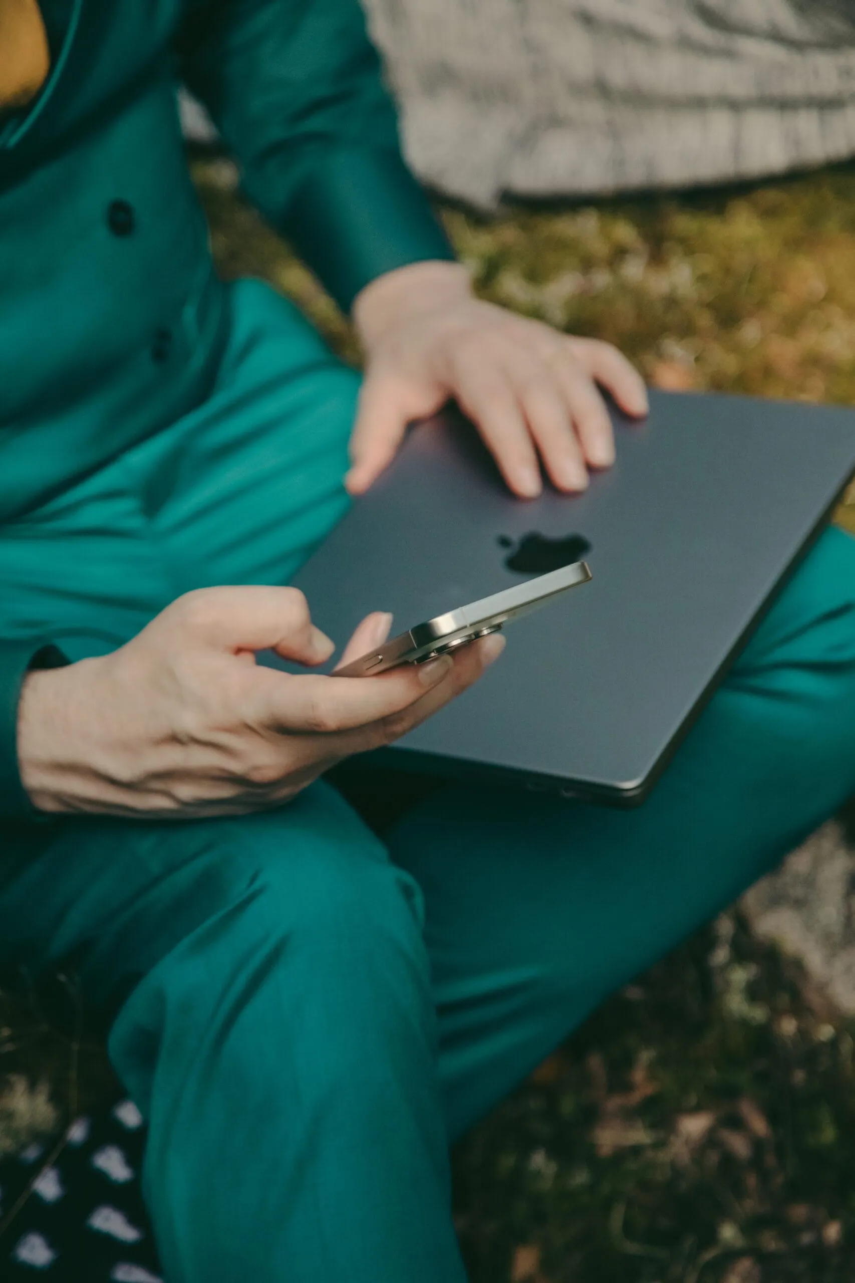 A person in a green suit holding a smartphone over a closed laptop outdoors.